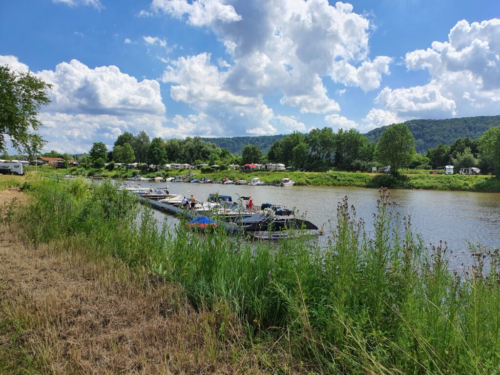 Lauenförde. Der Flecken Lauenförde treibt die Entwicklung eines neuen Freizeit- und Erholungsareals in unmittelbarer Nähe zum bestehenden Yachthafen „Dreiländereck“ voran. Im Mittelpunkt steht der Ankauf eines rund 24 Hektar großen Geländes, das derzeit noch vom Kieswerk Eggersmann genutzt wird. Der Gemeinderat wird am 3. Juli final über das Projekt abstimmen.
Ziel des Projekts ist es, das touristische Potenzial der Weserregion weiter auszuschöpfen und die Lebensqualität vor Ort nachhaltig zu steigern. Geplant sind unter anderem ein öffentlich zugänglicher Badesee mit Liegewiesen, zusätzliche Stellplätze für Wohnmobile sowie ein moderner Ausbau des bestehenden Campingplatzes. Unterstützt wird das Vorhaben vom Betreiber des Yachthafens, Wilfried Vössing.
„Ich freue mich über die Perspektive, hier in der Kiesgrube Lauenförde ein neues Freizeit- und Naherholungsgebiet entwickeln zu können. Gemeinsam wurden hier rechtzeitig die Weichen gestellt. Hier soll neben der Anlage eines Badestrandes auch die Erweiterung des Campingplatzes realisiert werden. Darüber hinaus ist der Plan, verschiedene Freizeitaktivitäten zu generieren. Ein toller Richtungszeig für eine positive Entwicklung des gesamten Dreiländerecks“, erklärte Gemeindedirektor Tino Wenkel gegenüber dem Täglichen Anzeiger Holzminden.
Wenkel ist zugleich Samtgemeindebürgermeister der Samtgemeinde Boffzen und hat in seiner bisherigen Amtszeit bereits zahlreiche Projekte in der Region initiiert und erfolgreich Fördermittel eingeworben. Seine Amtszeit könnte bald enden: Der erfahrene Verwaltungschef kandidiert derzeit für das Amt des Bürgermeisters der Stadt Beverungen. Die Wahl findet am 14. September statt.
Kernstück der aktuellen Pläne ist der Erwerb des Flurstücks 12/3 in der Gemarkung Lauenförde. Bereits im Jahr 2010 hatte sich das Unternehmen Eggersmann vertraglich verpflichtet, das Grundstück nach dem Ende des Kiesabbaus und der Rekultivierung an die Gemeinde zu veräußern. Diese Phase soll bis spätestens Ende 2026 abgeschlossen sein.
Neben dem Kauf des Geländes soll auch ein städtebaulicher Vertrag mit dem Campingplatzbetreiber abgeschlossen werden. Dieser sieht unter anderem die Übernahme von Planungs-, Erschließungs- und Kompensationskosten durch den Investor vor. Die Gemeinde verpflichtet sich im Gegenzug, das Vorhaben planungsrechtlich abzusichern.
Ein besonderes Augenmerk liegt auf der dringend notwendigen Verlagerung von Teilen des bestehenden Campingplatzes. Hintergrund sind neue Hochwasserprognosen für die Weser, die eine Nutzung bestimmter Flächen künftig ausschließen. Etwa 24.000 Quadratmeter sollen daher auf höher gelegenes Gelände verlegt werden.
Für die konkrete Ausgestaltung des Freizeitareals ist eine enge Zusammenarbeit mit der Firma Schröder Stellplatzplanung aus Bad Neuenahr-Ahrweiler geplant. Diese soll unter anderem eine Standortanalyse, eine Machbarkeitsstudie sowie eine Visualisierung der geplanten Anlage liefern. Auch unterschiedliche Betriebsmodelle für den zukünftigen Stellplatz sollen geprüft werden – von einfach bis voll digitalisiert.
Bereits zwischen 2008 und 2013 hatte das Planungsbüro SRL Weber aus Hannover erste Konzepte für das Gelände erarbeitet. Nun, mehr als ein Jahrzehnt später, könnte aus der Vision endlich Realität werden.
Die Gemeinde Lauenförde sowie die Samtgemeinde Boffzen planen, frühzeitig Fördermittel zu beantragen, um die Entwicklung des Areals auch finanziell abzusichern. „Wir schaffen hier nicht nur ein attraktives Freizeitangebot, sondern investieren in die Zukunft unserer Region“, resümiert Wenkel. Jetzt bleibt es abzuwarten, wie die Politik in der Gemeinderatssitzung über dieses Großprojekt abstimmt und dann ähnlich, wie in Godelheim eine Freizeitanlage mit Badesee im Dreiländereck entsteht?

