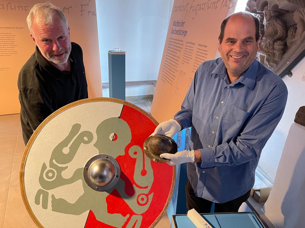 Georg Egenstein ist Kurator der Ausstellung und zeigt hier mit dem Stadtarchologen Ralf Mahtka ein besonderes Exponat, ein Schildbuckel